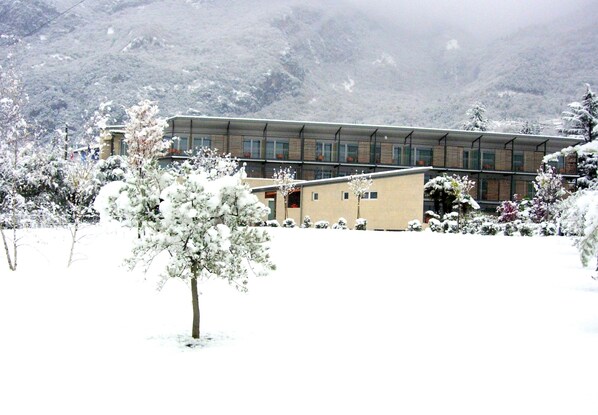 A building with a flat roof and large windows, surrounded by snow-covered trees and mountains.