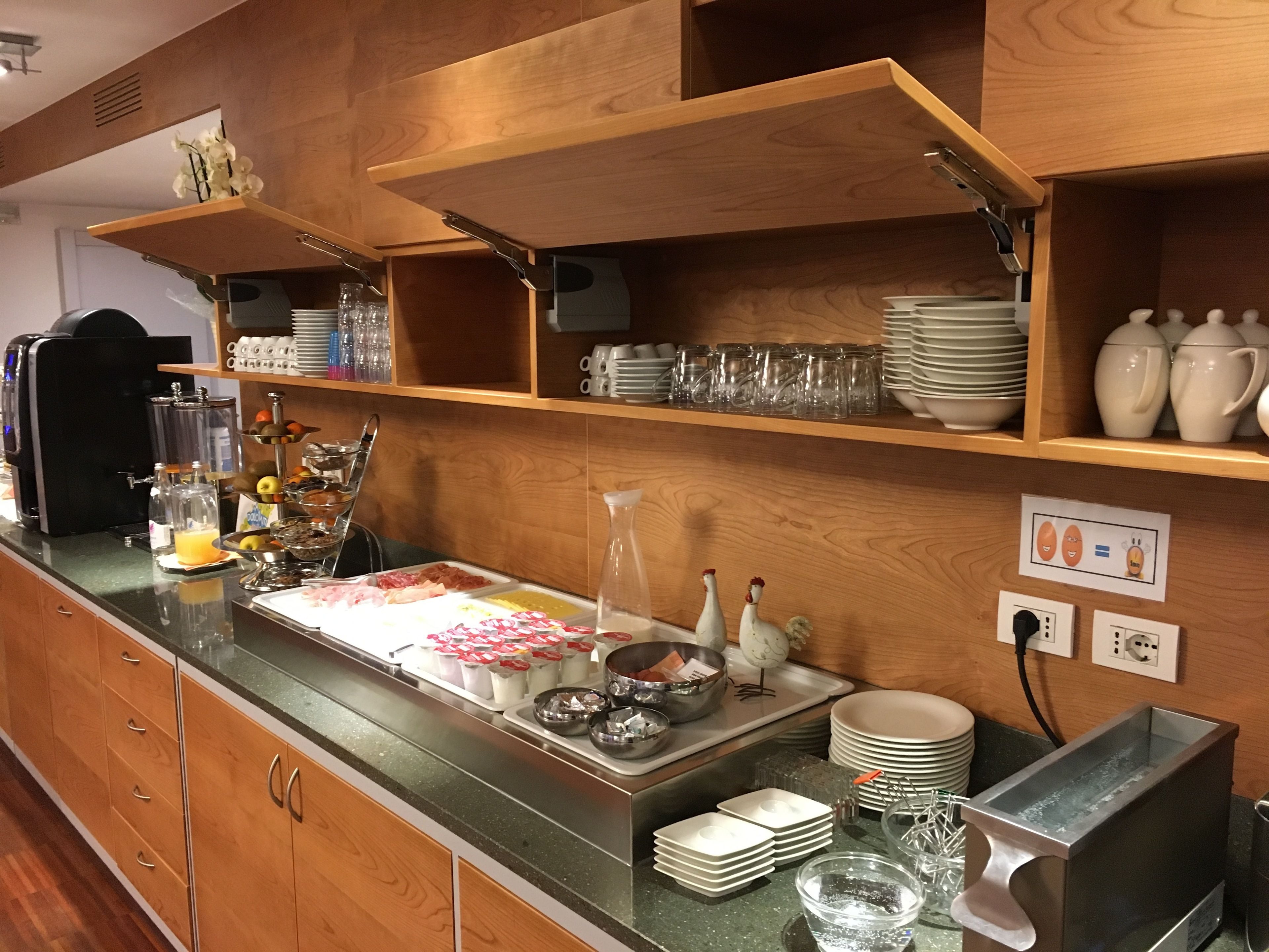 Una barra de desayuno con una máquina de café, una exhibición de frutas y diversos productos para el desayuno.