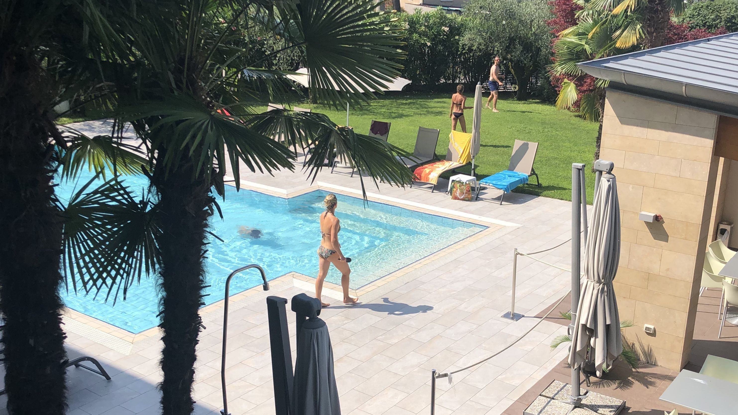Una piscina con solárium de baldosas, rodeada de palmeras y sillones de descanso.