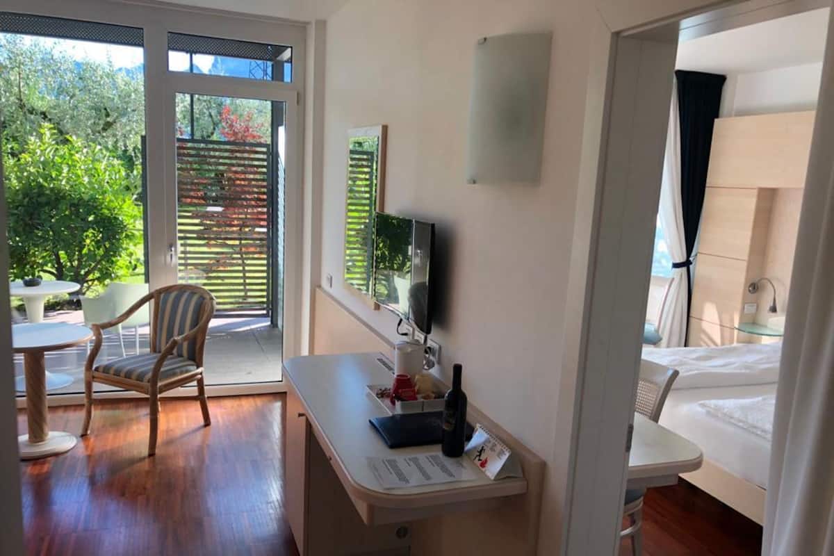 A hotel room with a desk, chair, bed, and a balcony with a table and chairs.