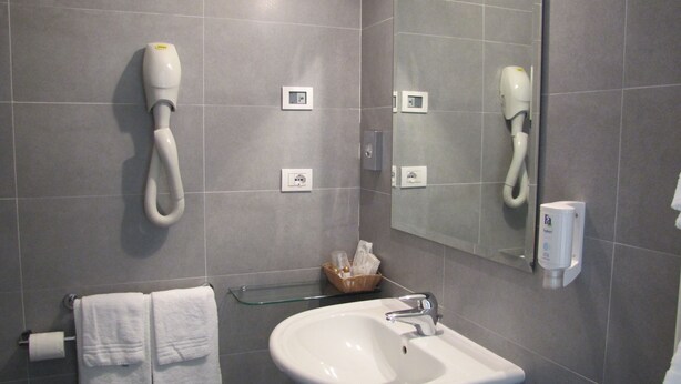 A bathroom with a white sink, a mirror, a towel rack, and a hairdryer mounted on the wall. - Park Hotel Il Vigneto (Arco)