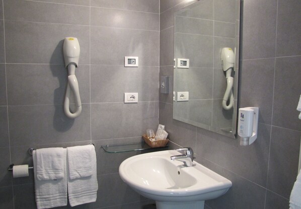 Un baño con un lavamanos blanco, un espejo, un perchero y un secador de pelo fijado en la pared.