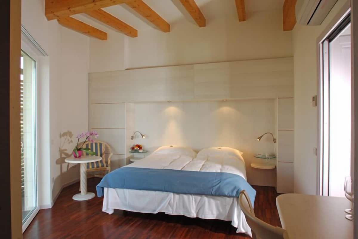 A bedroom with a large bed, bedside tables, a chair, and a small table with a vase of flowers.
