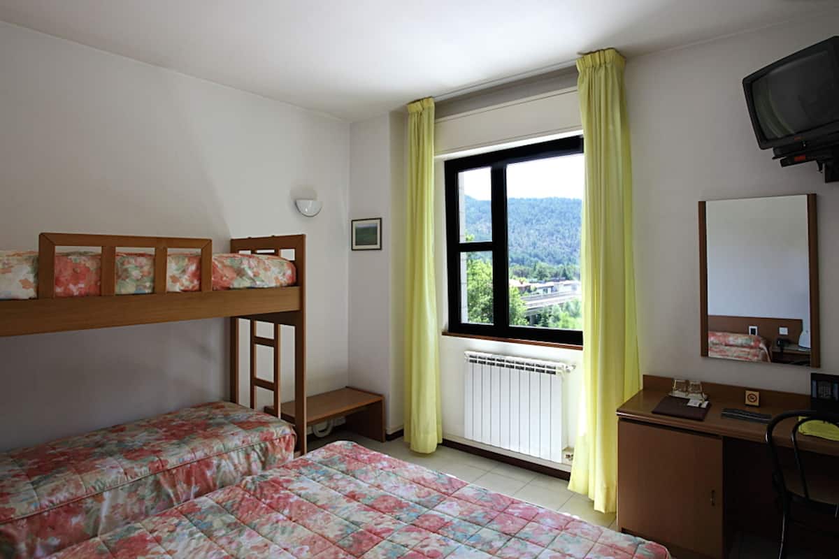A room with bunk beds, a desk, a chair, a window with curtains, a radiator, and a television.