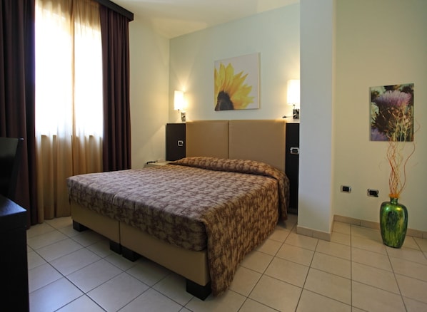 A hotel room with a large bed, two bedside tables, a nightstand, a TV, a window with curtains, and artwork on the walls. - Euro Hotel (Pieve Santo Stefano)