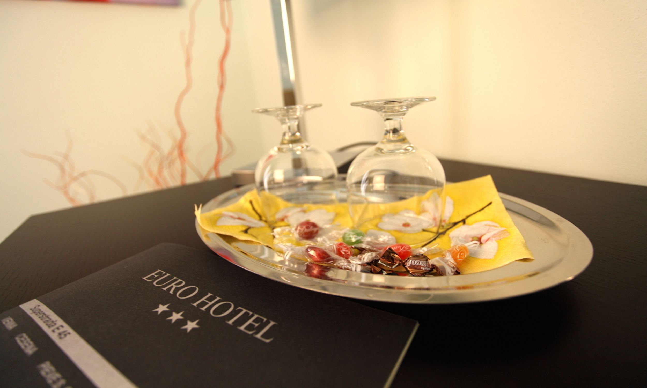 A table with a glass tray holding various candies and a glass bottle, with a "EURO HOTEL" sign on the table.