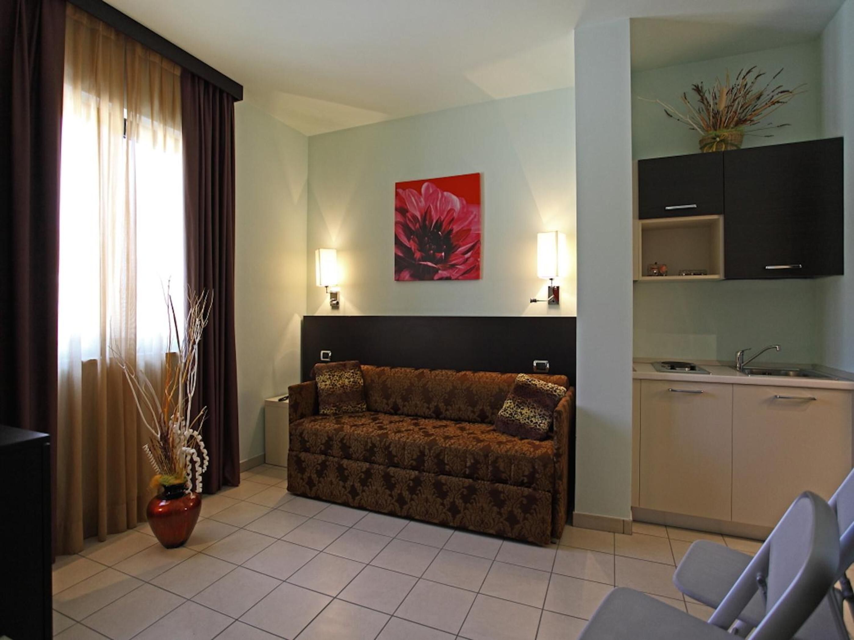 A living room with a sofa, a coffee table, a TV, and a plant. There is a kitchen area with cabinets and a sink.