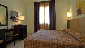 Une chambre d’hôtel comprenant un lit, un bureau avec une chaise, une télévision et une fenêtre avec des rideaux.