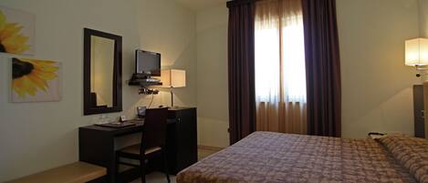 Una habitación de hotel con una cama, un escritorio con una silla, un televisor y una ventana con cortinas.