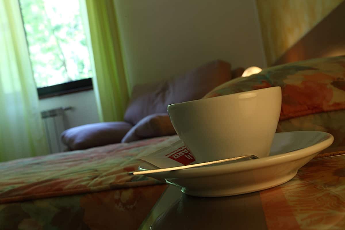 A cup on a saucer on a table in a room with a window, a couch, and a radiator.