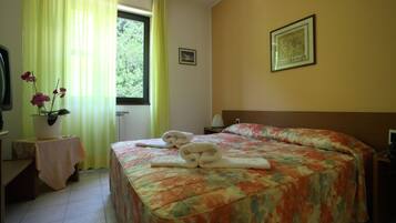 Ein Hotelzimmer mit einem Bett, einem Nachttisch, einem Tisch mit Blumenvase und einem Fenster mit Vorhängen.