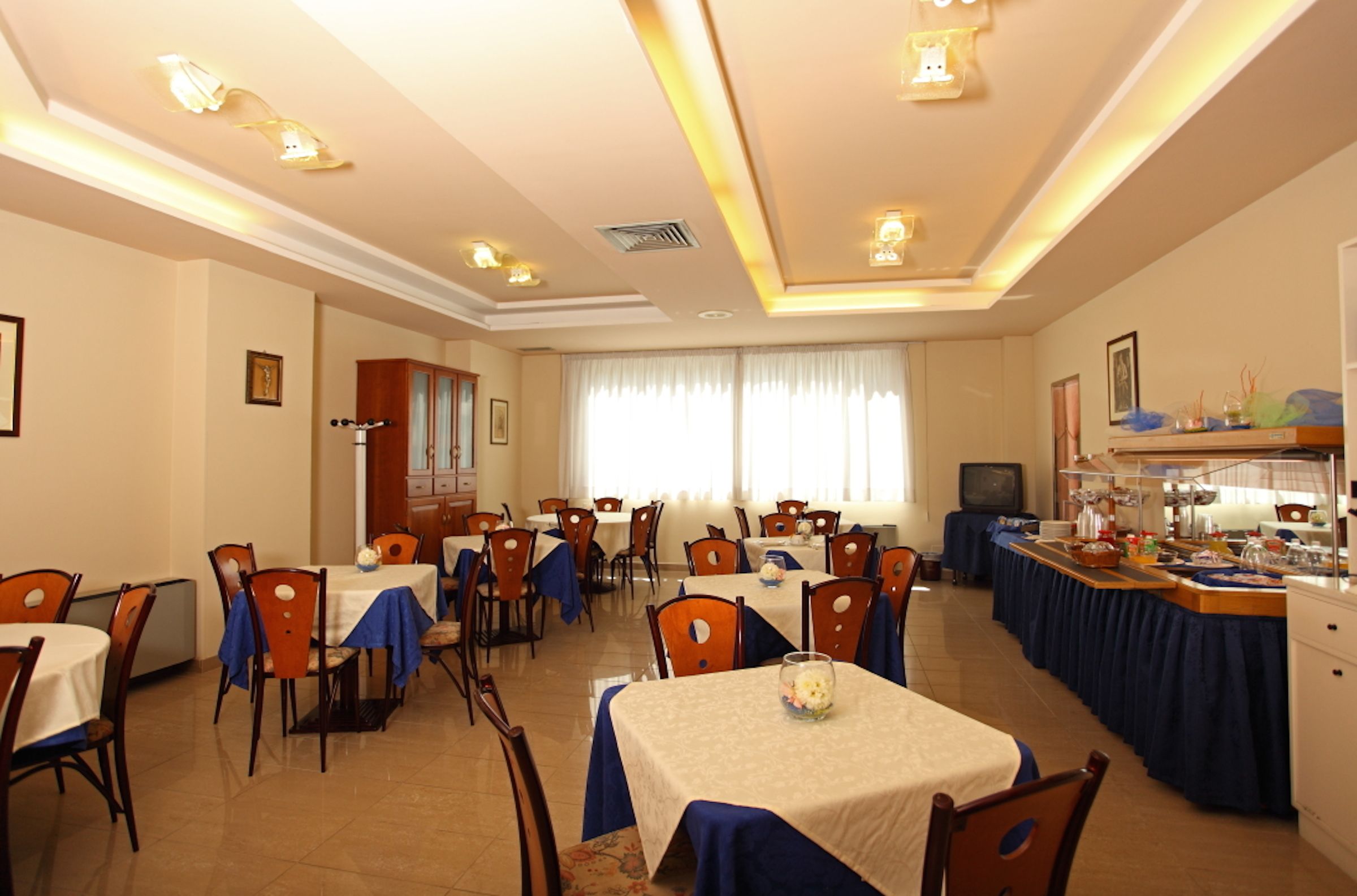 Uma área de refeições com várias mesas e cadeiras, um buffet e uma televisão sobre um suporte.