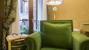 Un fauteuil vert avec un coussin, une lampe, une fenêtre avec des rideaux et une petite table sur laquelle se trouvent des verres et un livre.