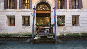Il s'agit d'un bâtiment historique doté d'une façade en pierre, d'une porte en bois avec une fenêtre en arc de cercle et d'un petit espace extérieur aménagé avec une table et des chaises.