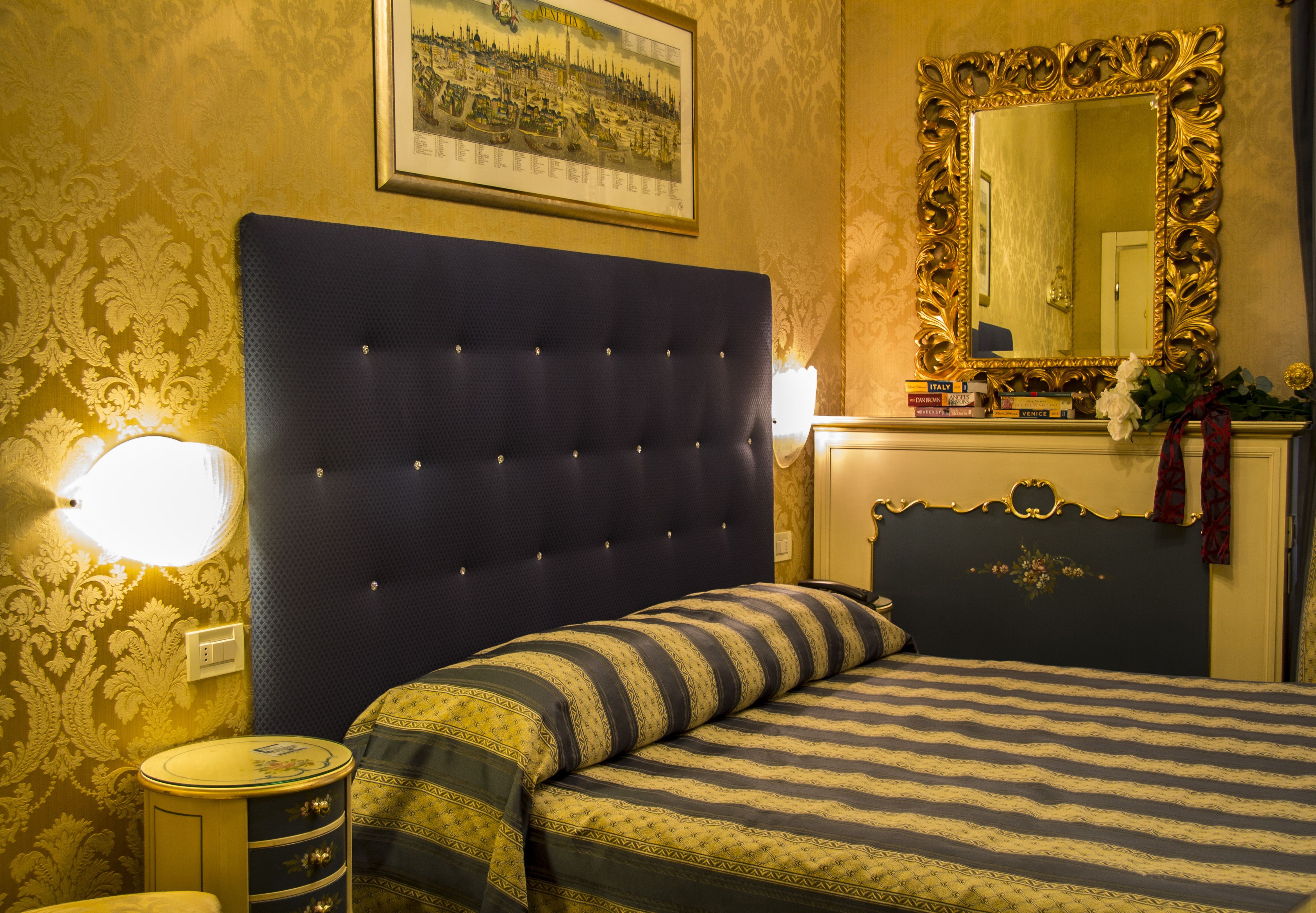 A bedroom with a tufted headboard, a bed with striped bedding, a round bedside table, a mirror, and a framed picture on the wall.