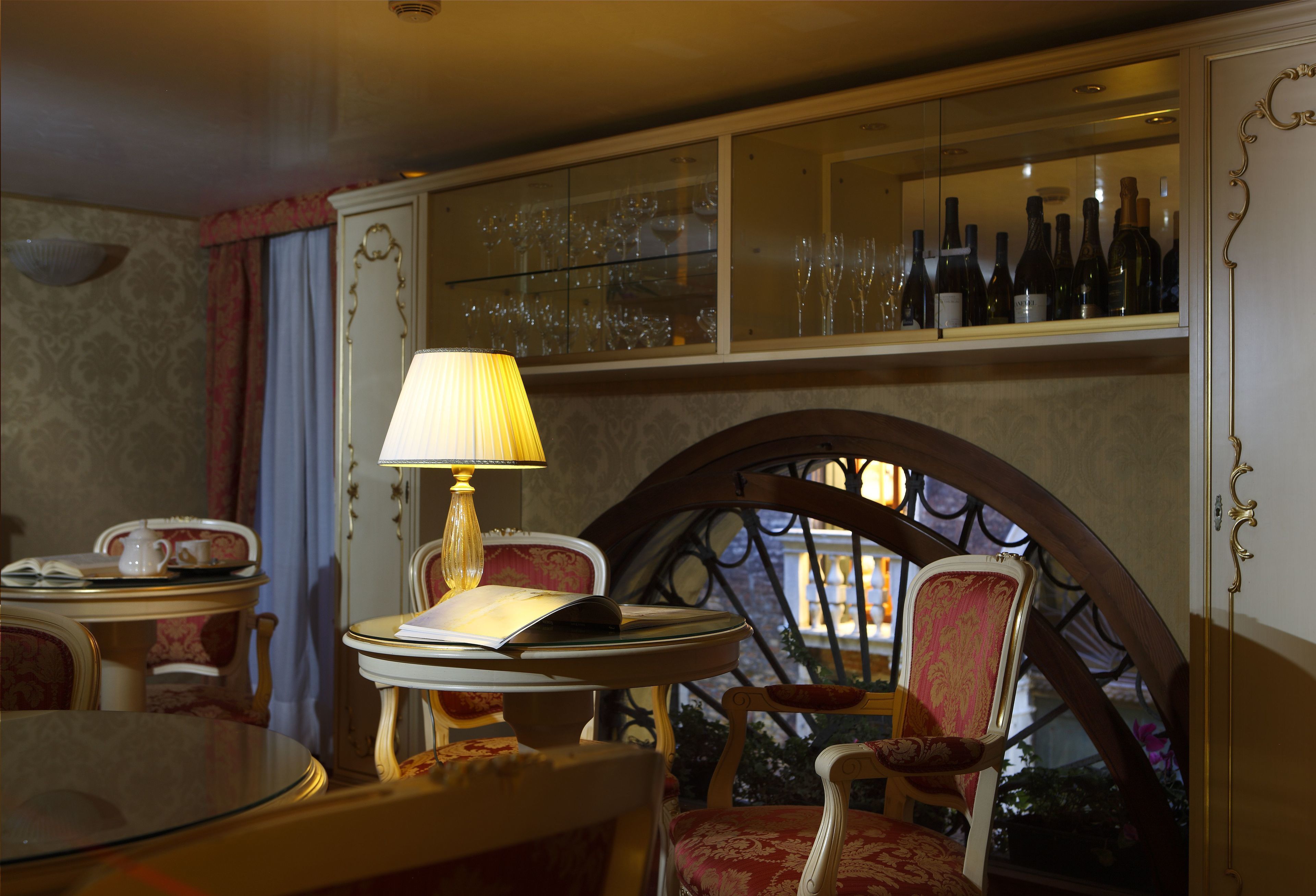 Un comedor con una mesa redonda, sillas, una lámpara y una estantería para vinos con botellas.
