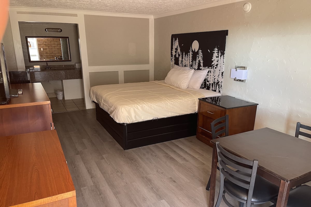 A compact bedroom with a bed, a small desk, a chair, and a kitchenette area.