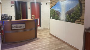 A reception desk with a 'Welcome' sign, a wall-mounted painting of a waterfall, and a brick wall. - Stratford House Inn Branson (Branson)