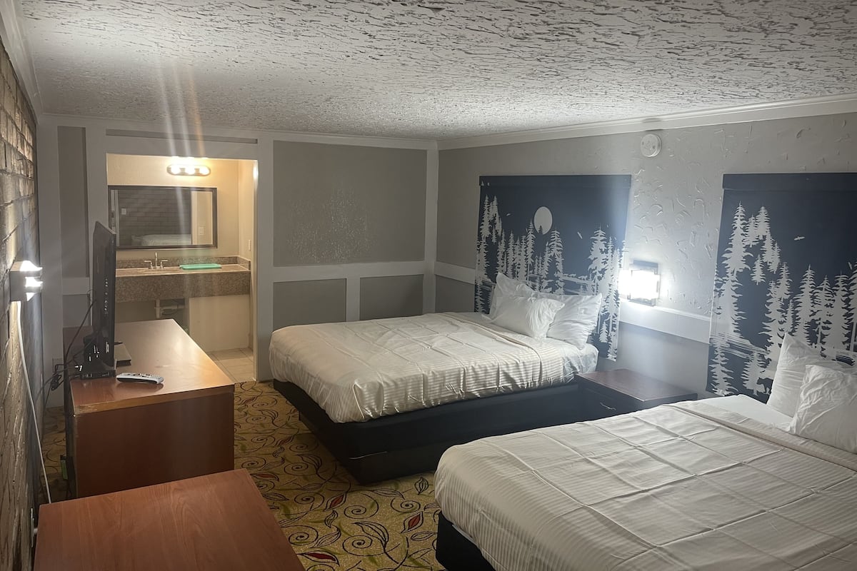 A hotel room with two beds, a bathroom with a mirror, and a TV on a wooden table.