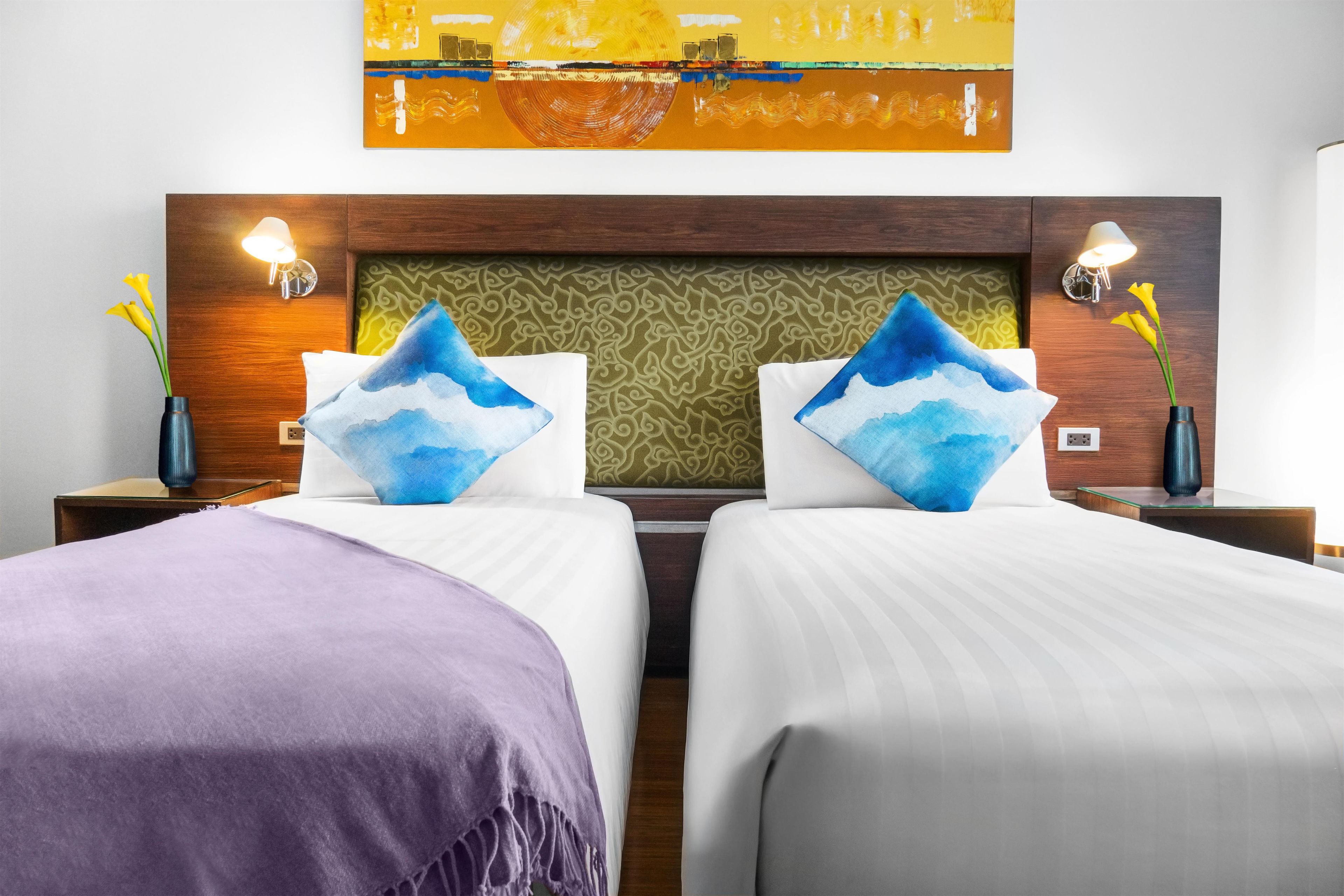 Habitación de hotel con dos camas, un cabecero estampado y lámparas fijadas a la pared.