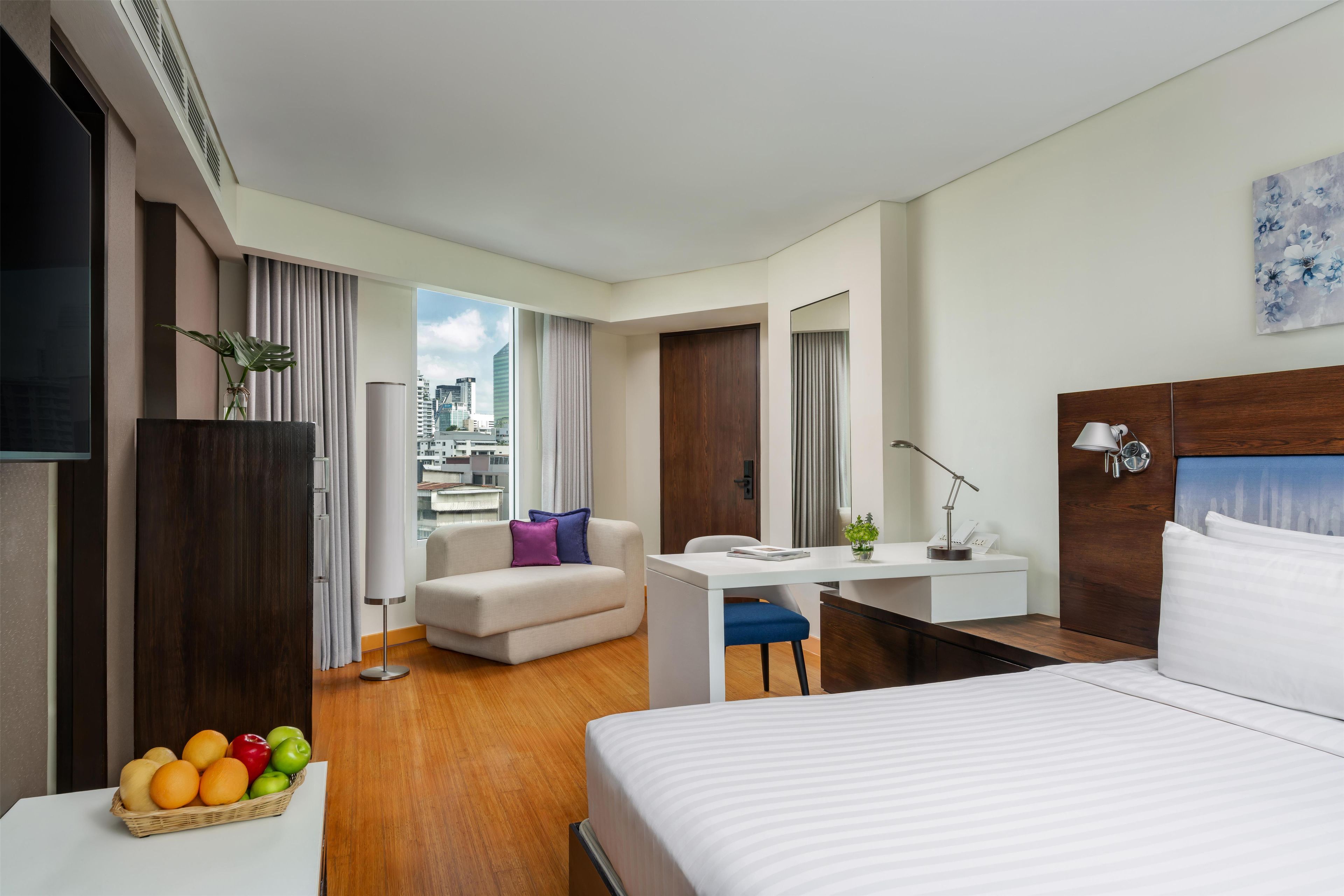 A hotel room with a bed, a desk, a sofa, and a view of the cityscape.