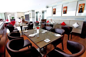 Un espace de restauration moderne avec des tables préparées pour deux personnes, des fauteuils en cuir et un assortiment de coussins décoratifs rouges et blancs.