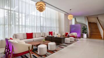 A modern living room with a sofa set, coffee table, ottomans, and a staircase.