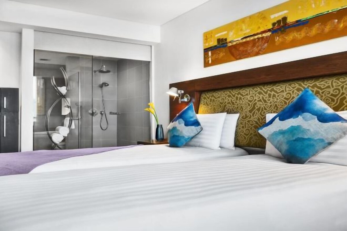 A hotel room with a bed, a shower area, and a large painting on the wall.