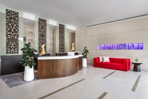 A reception area with a wooden reception desk, a red sofa, and decorative panels on the walls. - NH Bangkok Asoke (Bangkok)