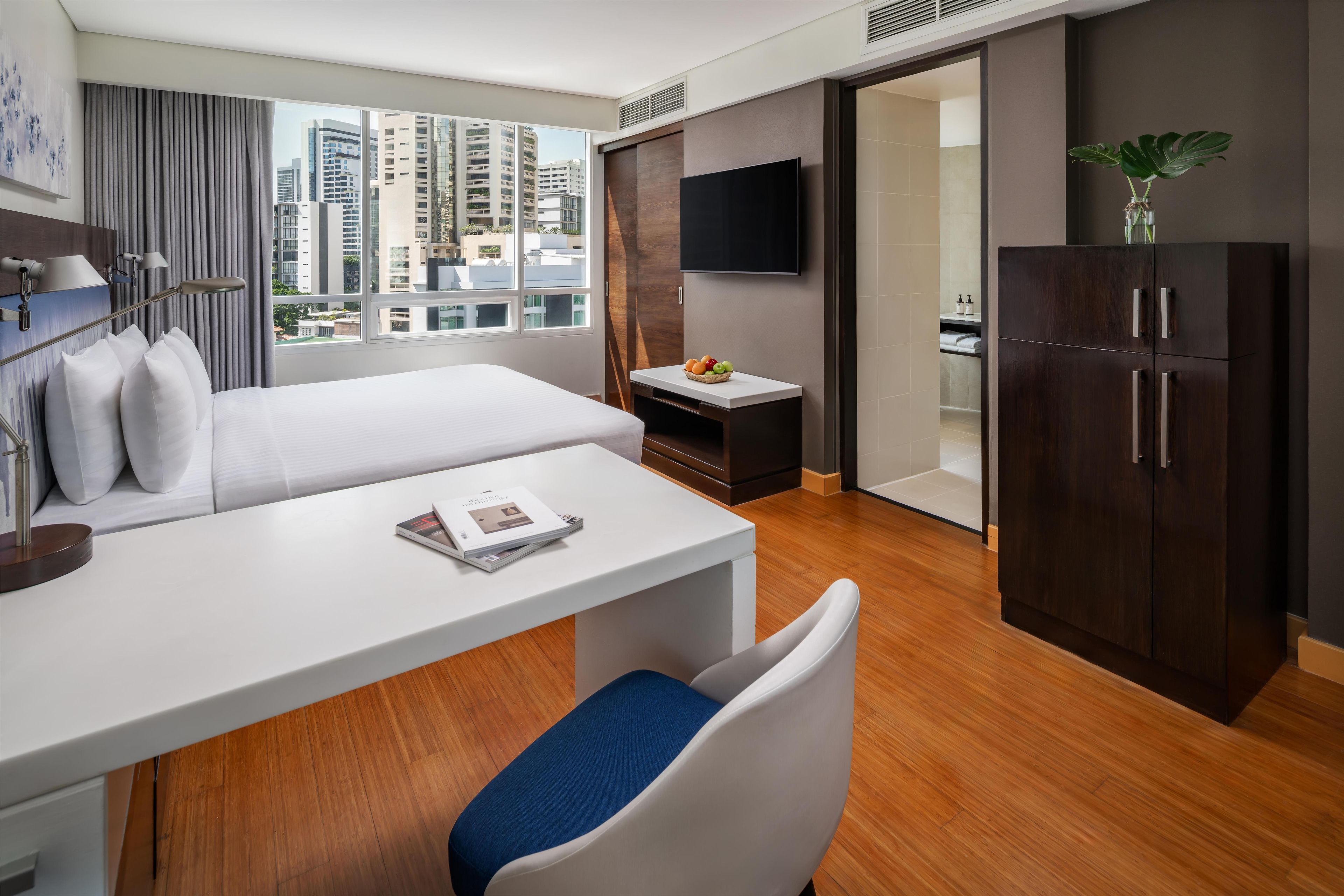 Une chambre d’hôtel moderne équipée d’un lit, d’un bureau, d’une chaise, d’une télévision et d’une armoire.
