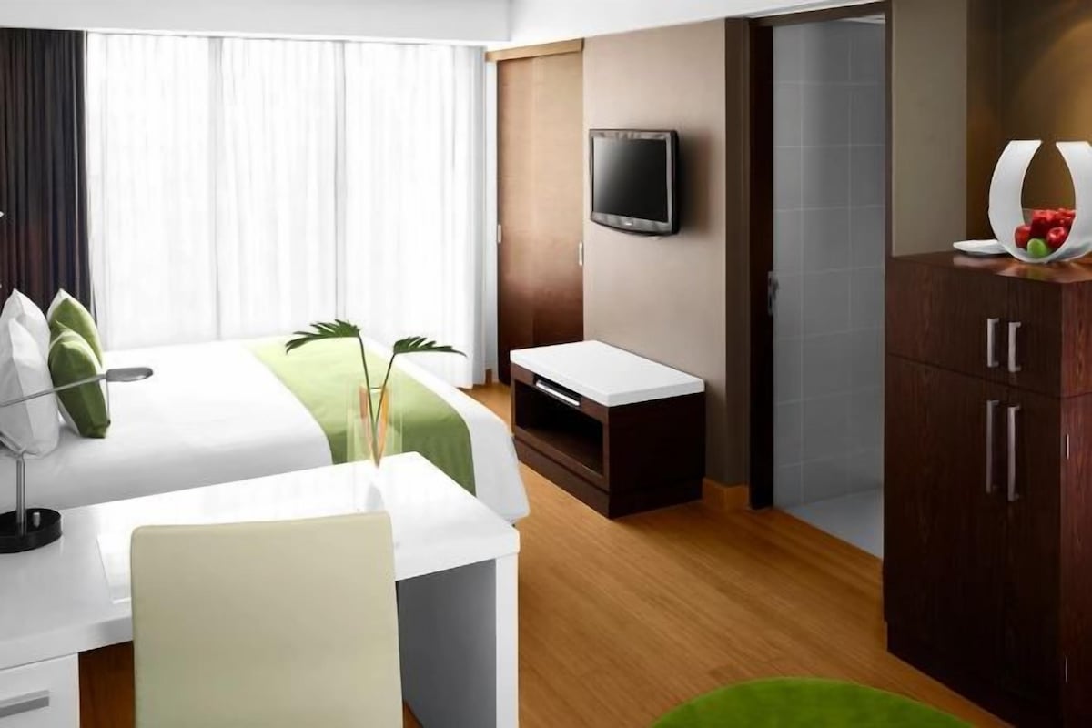 A hotel room with a bed, a desk, a TV, and a cabinet.