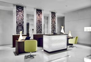 A modern reception area with a reception desk, two chairs, and decorative panels. - NH Bangkok Asoke (Bangkok)