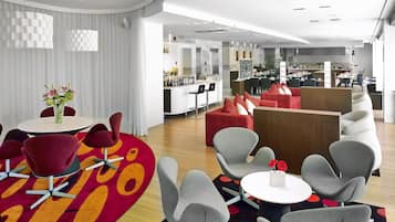 A modern hotel lobby with a bar area, seating arrangements, and a visible kitchen in the background.