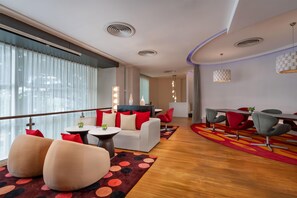 A modern hotel lobby with a sofa, chairs, a dining area, and a large window with curtains. - NH Bangkok Asoke (Bangkok)