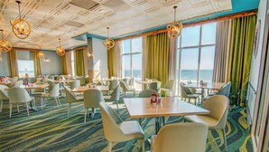 A hotel dining area with tables and chairs, large windows with curtains, and a patterned carpet. - Sea Watch Resort (Myrtle Beach)