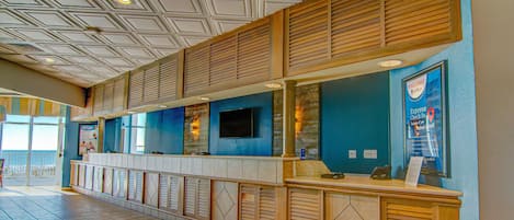 Zona de recepción con mostrador de check-in, televisor de pantalla plana y pared azul.
