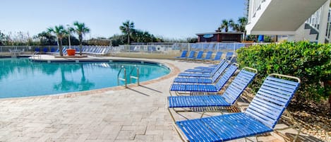 A swimming pool with blue lounge chairs and a tiled deck.