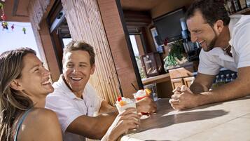 A group of people sitting at a bar with drinks, a tiled floor, and a brick wall.