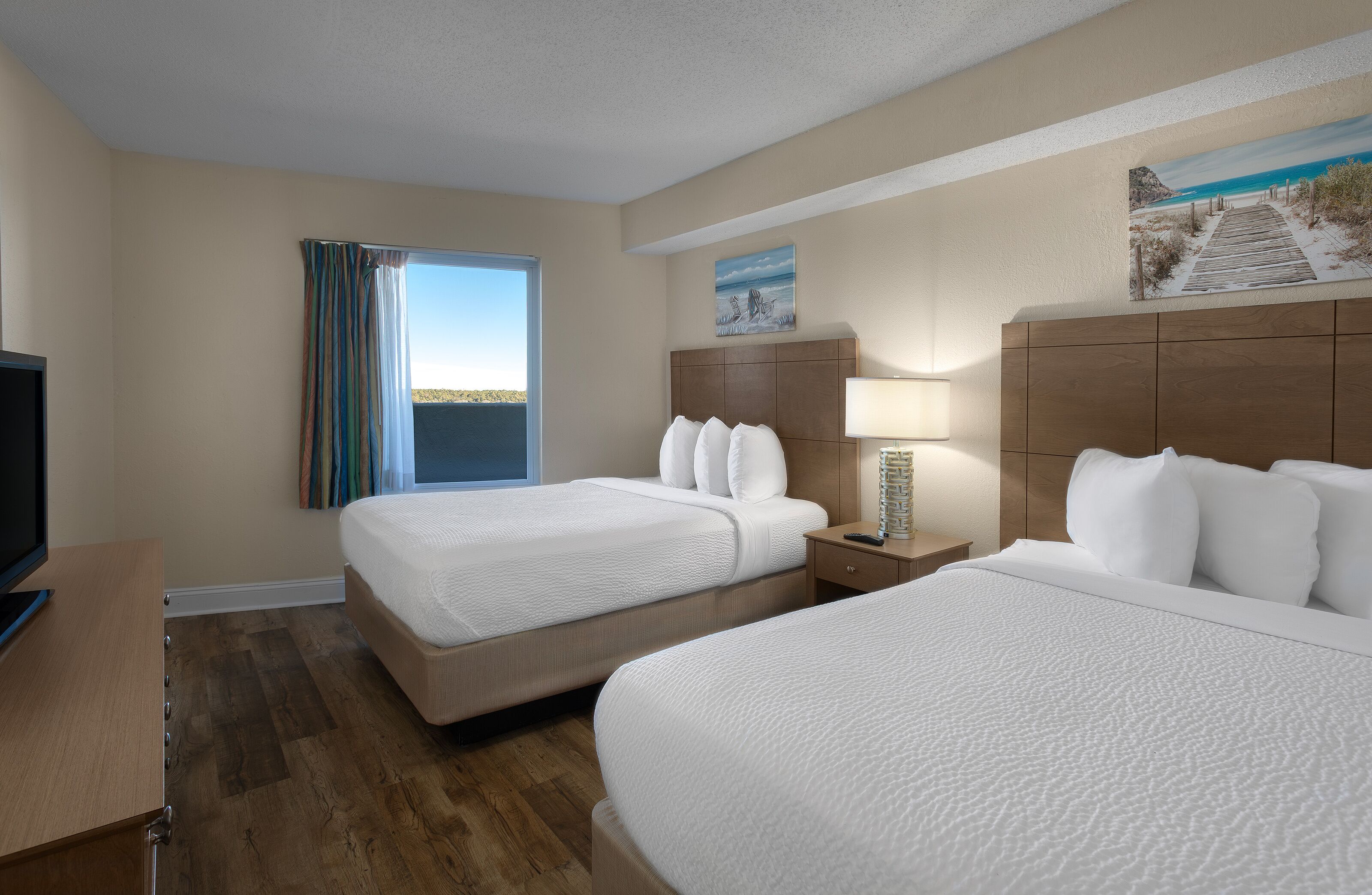 A hotel room with two beds, a TV, a desk, and a window with curtains.