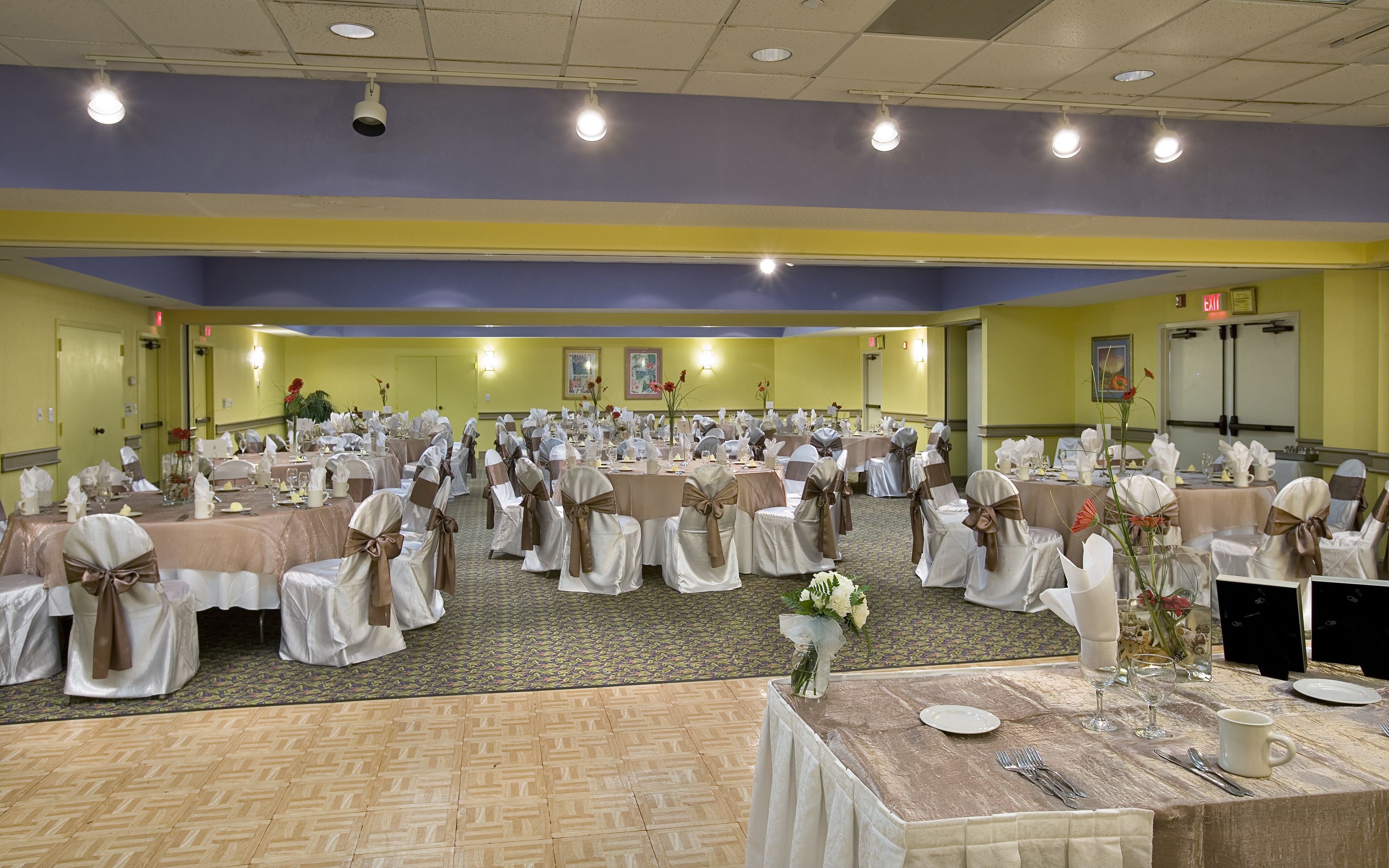 A banquet hall with round tables, chairs, and floral centerpieces.