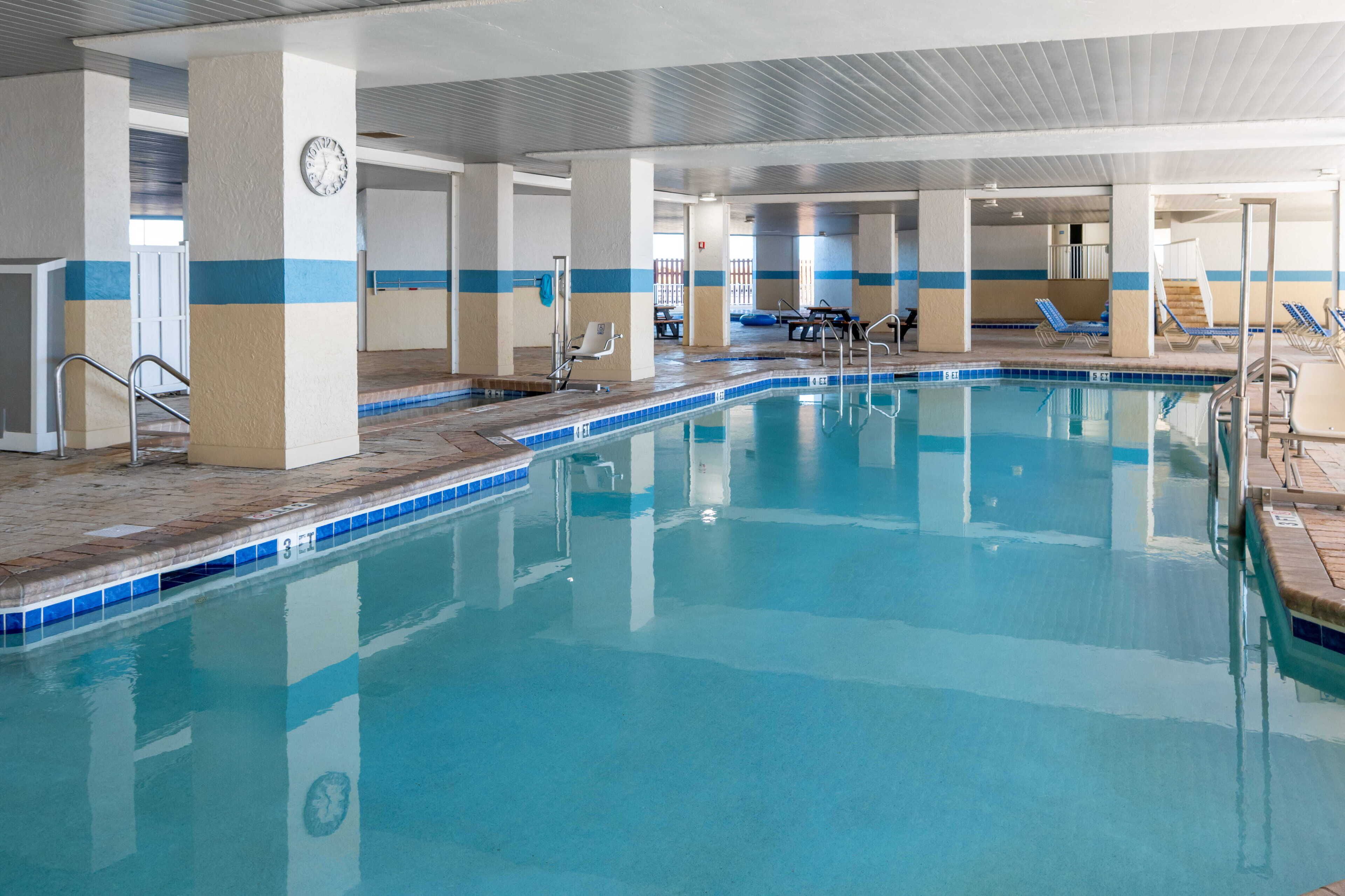An indoor swimming pool with clear blue water, tiled edges, and a clock on a pillar.