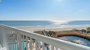 A balcony with a view of a beach, a pool, and a boardwalk. - Sea Watch Resort (Myrtle Beach)