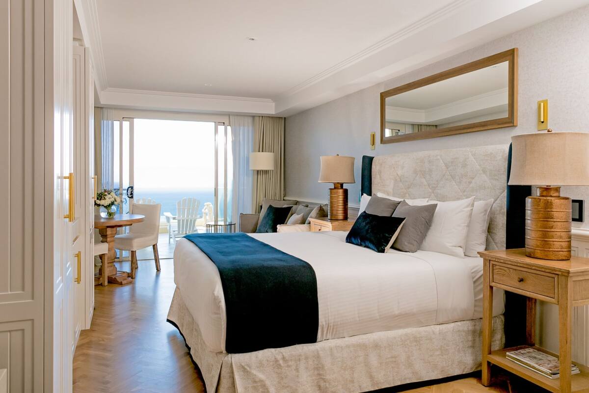 A hotel room with a large bed, two bedside tables, a mirror, and a view of the ocean.