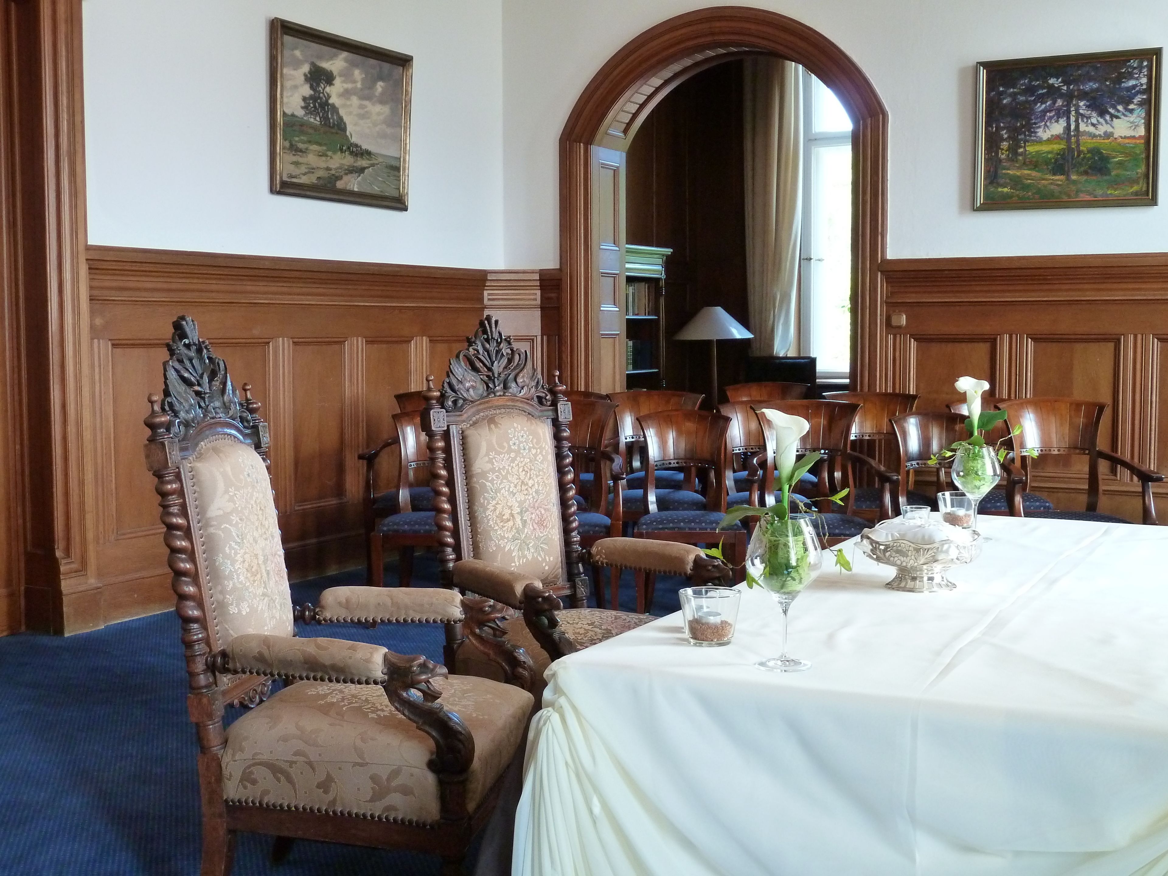 A formal dining room with ornate wooden chairs, a white tablecloth, and floral centerpieces.