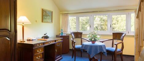 A room with a wooden desk, a chair, a table with a blue tablecloth, and a window with curtains.