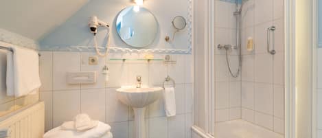 A bathroom with a pedestal sink, a mirror, a towel rack, a shower area, and a radiator.