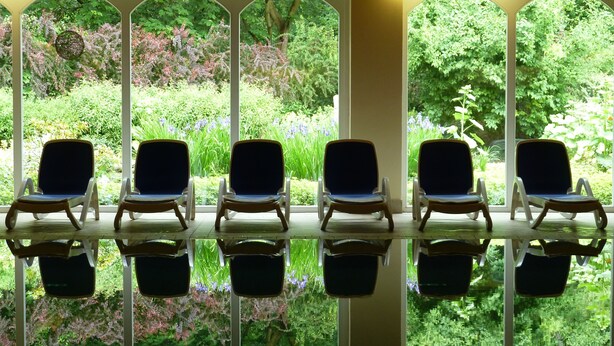 A row of five lounge chairs with a glass table reflecting the surrounding greenery. - Schlosshotel Ralswiek (Ralswiek)
