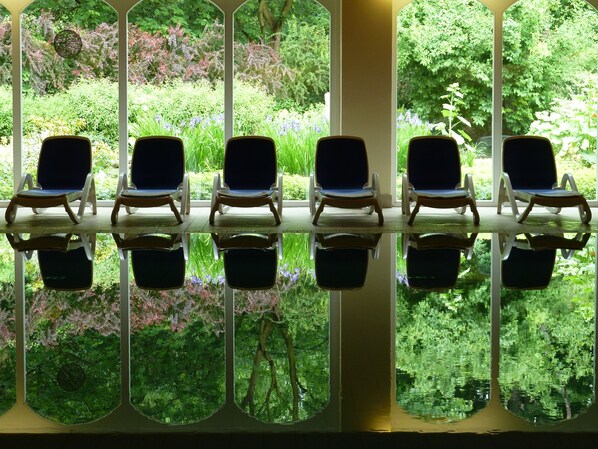 A row of five lounge chairs with a glass table reflecting the surrounding greenery. - Schlosshotel Ralswiek (Ralswiek)
