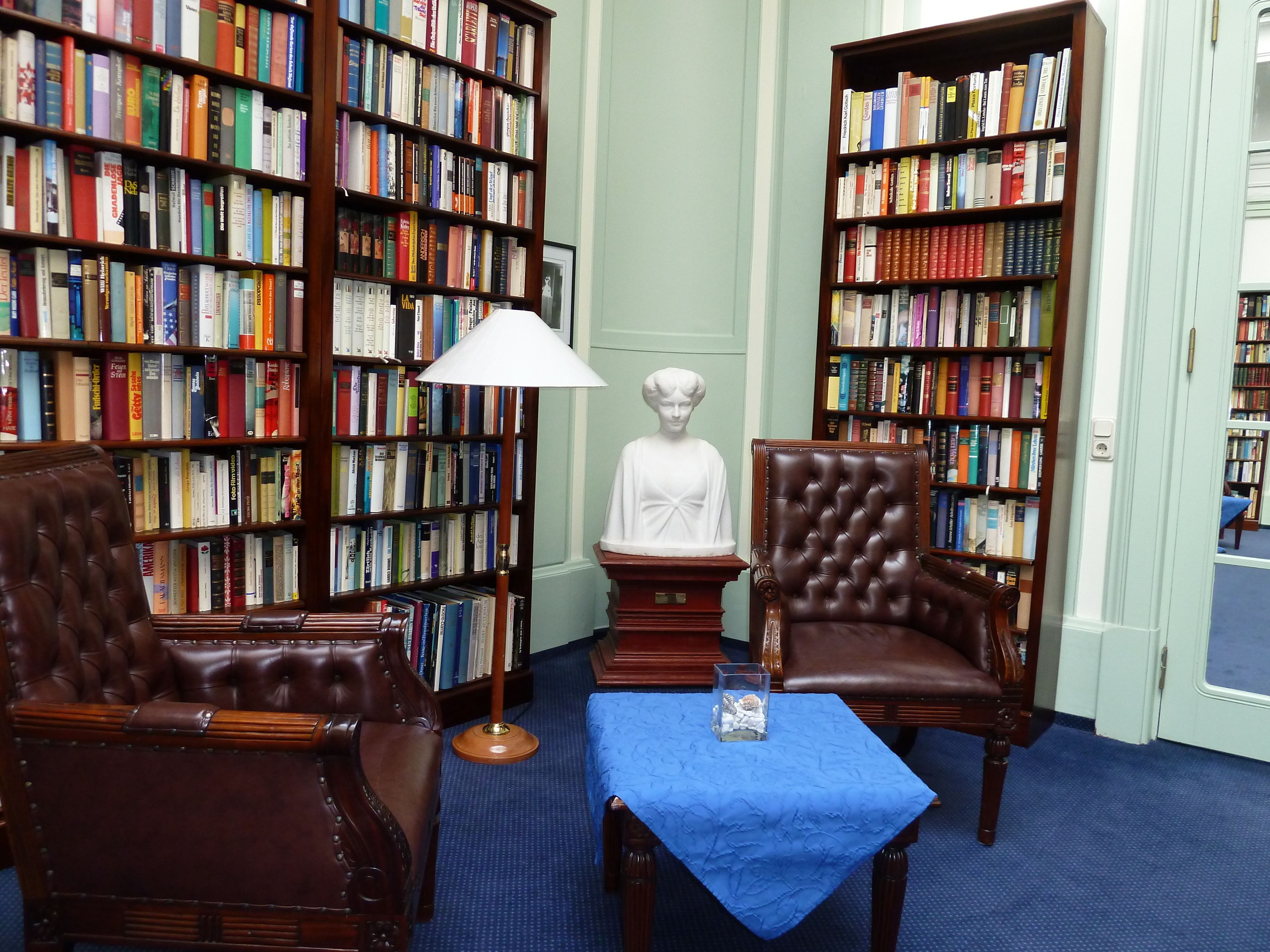 A library with leather chairs, a bust sculpture, and a blue table.