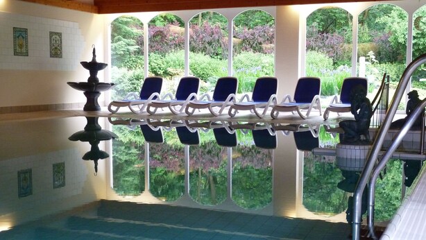 An indoor swimming pool with a clear view of the surrounding garden through arched windows. - Schlosshotel Ralswiek (Ralswiek)